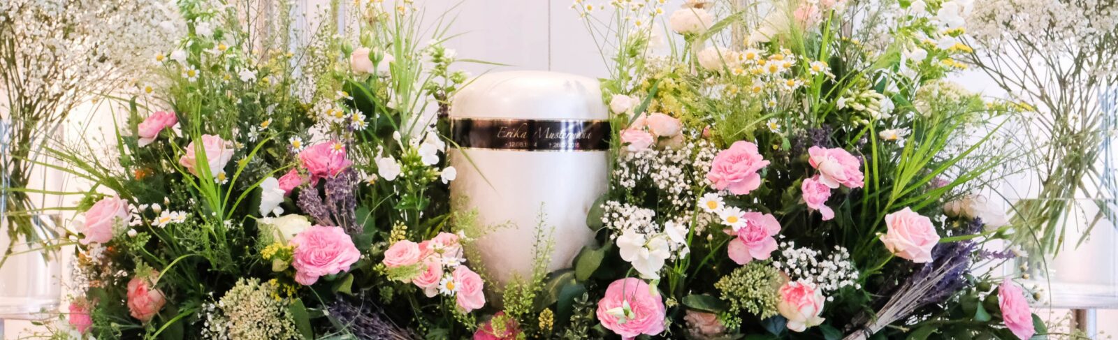 GBI Hamburg Bestatter Moderne Urne auf einen rosafarbenen Blumengesteck